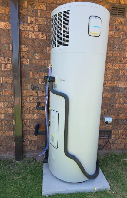  A tall, white Aquatech heat pump hot water system installed on a concrete slab against a red brick exterior wall with insulated plumbing