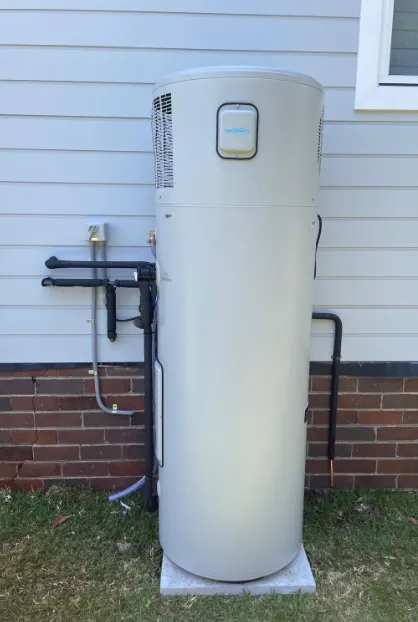 An aquatech heat pump water heater installed outdoors on a concrete base against a brick exterior wall